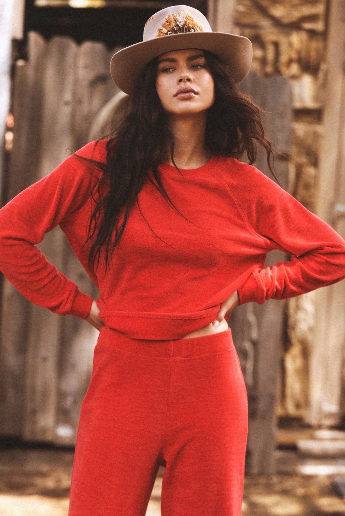 Woman in a red outfit with a hat standing in front of a rustic wooden background