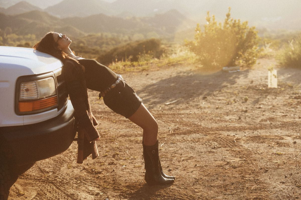 Person leaning against a white truck in a desert setting with mountains in the background